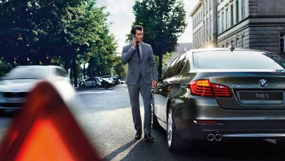 Служба помощи на дороге BMW Roadside Assistance Служба помощи на дороге BMW Roadside Assistance, мужчина разговаривает по телефону перед автомобилем BMW