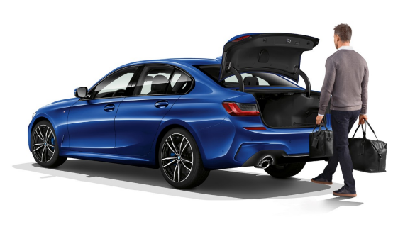 Седан BMW 3 серии, функция автоматического открывания крышки багажного отделения Вид седана BMW 3 серии сзади с поворотом в три четверти, водитель приводит в действие функцию автоматического открывания крышки багажного отделения движением ноги.