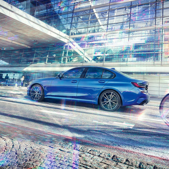 Седан BMW 3 серии, вид сбоку Стоп-кадр седана BMW 3 серии сбоку в дневное время на фоне здания со стеклянным фасадом.