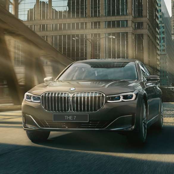 BMW 7 серии: системы помощи водителю Системы помощи водителю: седан BMW 7 серии в движении на фоне городского пейзажа