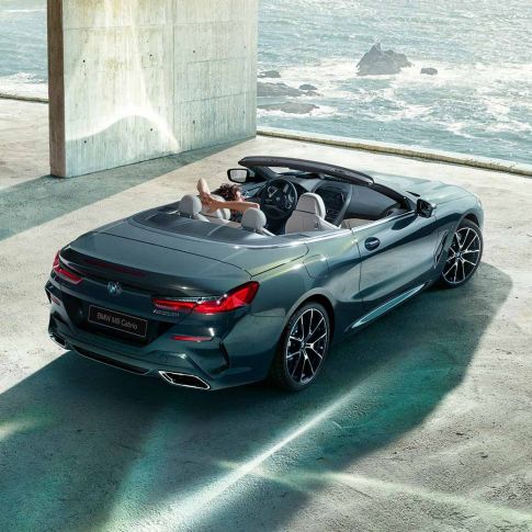 BMW M850i xDrive Cabrio, вид с высоты птичьего полета. BMW M850i xDrive Cabrio с открытым мягким верхом, Серый Дравит металлик, вид с высоты птичьего полета, паркуется в здании из бетона перед океаном.