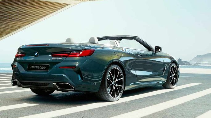 BMW M850i xDrive Cabrio, вид сзади с поворотом в три четверти. BMW M850i xDrive Cabrio с открытым мягким верхом, Серый Дравит металлик, вид сзади с поворотом в три четверти, автомобиль паркуется на фоне океана.