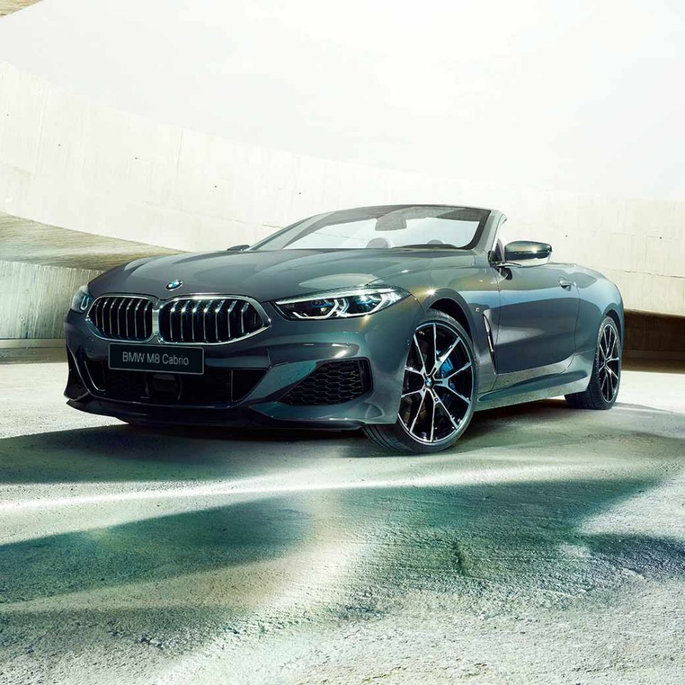 BMW M850i xDrive Cabrio, вид спереди с поворотом в три четверти. BMW M850i xDrive Cabrio с открытым мягким верхом, Серый Дравит металлик, вид спереди с поворотом в три четверти, неподвижный автомобиль в здании из бетона.