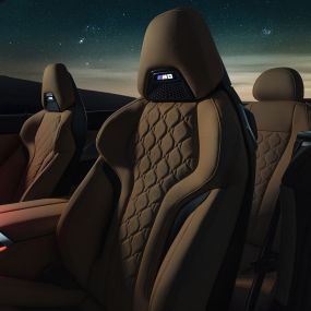 Спортивные сиденья M с обивкой из кожи Merino. BMW M8 Competition Cabrio с открытым мягким верхом под звездным небом, интерьер с акцентом на спортивные сиденья M с обивкой из кожи Merino и фоновой подсветкой красного цвета.