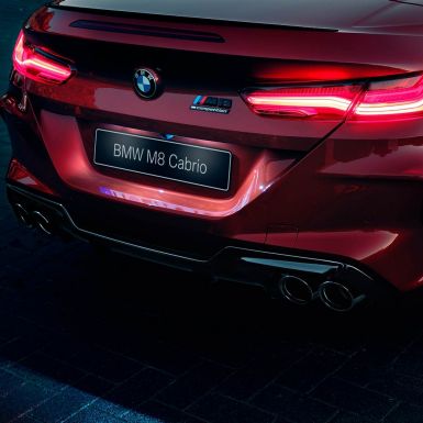 BMW M8 Competition Cabrio, крупный план задней части кузова. BMW M8 Competition Cabrio, Красный Мотеги металлик, крупный план задней части кузова с акцентом на светодиодные задние фонари и эмблему M8 Competiton.