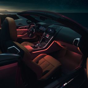 BMW M8 Competition Cabrio, интерьер. BMW M8 Competition Cabrio с открытым мягким верхом, интерьер с фоновой подсветкой красного цвета в темное время суток.