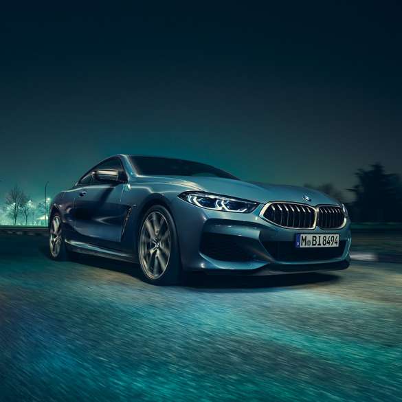 BMW M850i xDrive Coupe, вид спереди слева с поворотом в три четверти. BMW M850i xDriveCoupe, Синий Барселона металлик, вид спереди слева с поворотом в три четверти, автомобиль в движении в темное время суток.