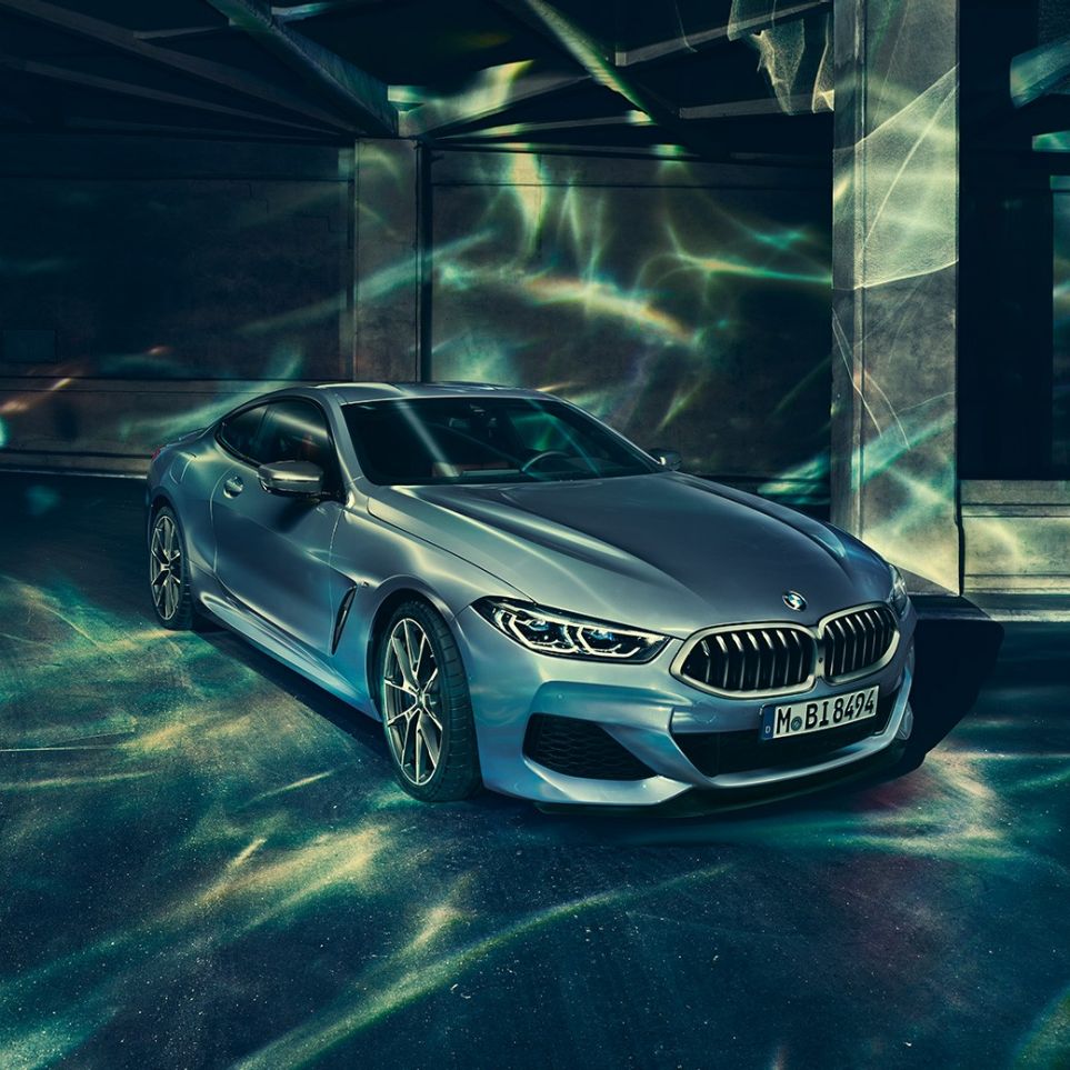 BMW M850i xDriveCoupe, вид спереди слева с поворотом в три четверти. BMW M850i xDriveCoupe, Синий Барселона металлик, вид спереди слева с поворотом в три четверти, неподвижный автомобиль перед зданием.