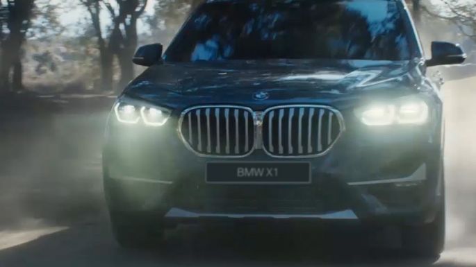 BMW X1 в движении, вид спереди с поворотом в три четверти на фоне природного пейзажа.