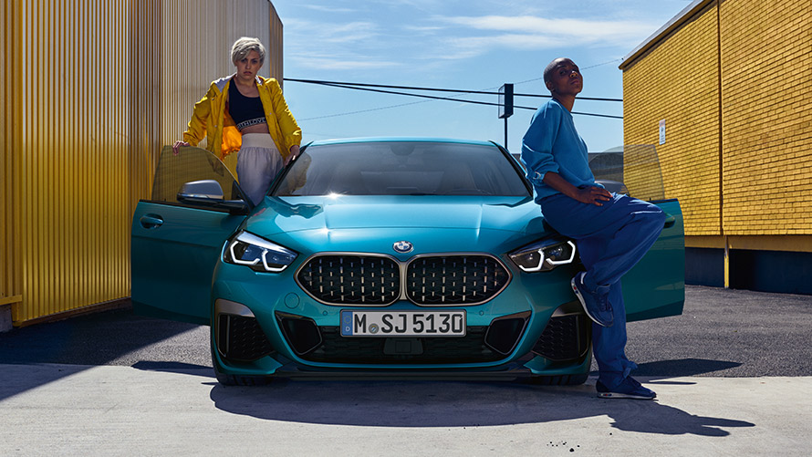 BMW 2 серии Gran Coupe F44, вид спереди BMW 2 серии Gran Coupe F44, Синий Снэппер Рокс, вид спереди с открытыми дверями и двумя человеками у автомобиля