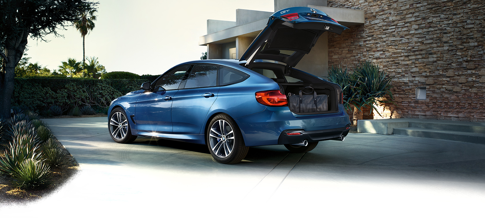 BMW 3 серии Гран Туризмо, вид сзади с поворотом в три четверти. BMW 3 серии Гран Туризмо, вид сзади с поворотом в три четверти, открытый багажник, на даче, за городом.