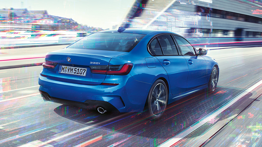 Вид сзади в три четверти BMW 3 серии (G20) днем на урбанистическом фоне.