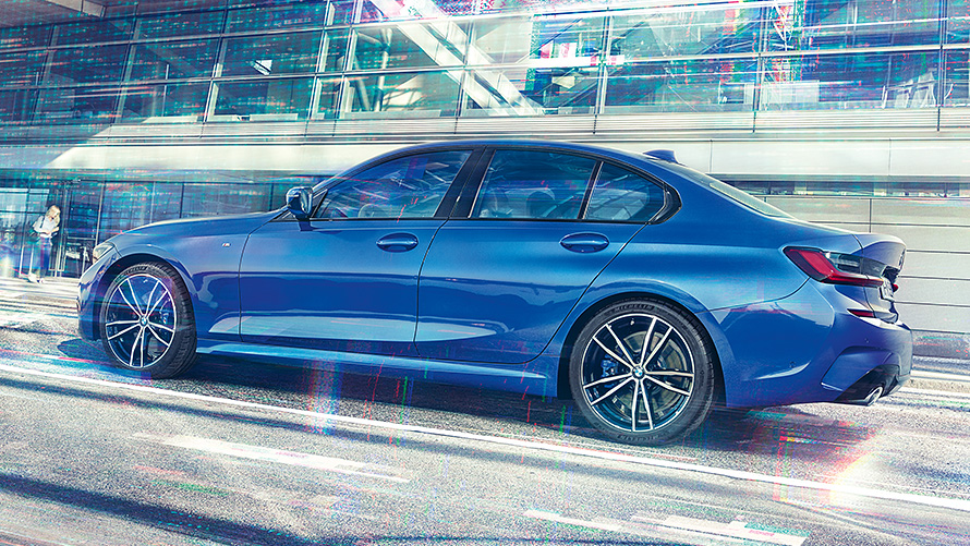 Вид сбоку в статике BMW 3 серии (G20) цвета &quot;Синий Портимау&quot; днем перед зданием из стекла.
