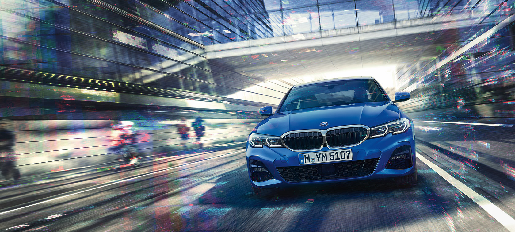 Вид спереди BMW 3 серии (G20) днем под стеклянным зданием.