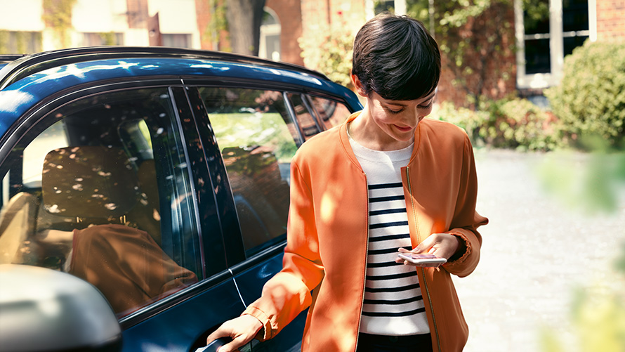 Сервис BMW, женщина со смартфоном рядом с дверью своего BMW Сервис BMW, женщина со смартфоном рядом с дверью своего BMW