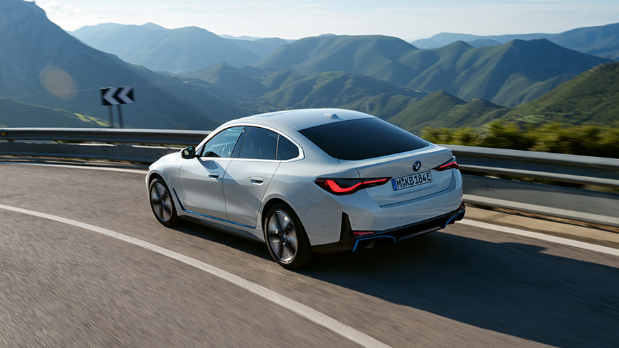 Вид сзади в три четверти BMW i4 eDrive40 G26 2021 в движении BMW i4 eDrive40 G26 2021 "Белый Минерал", вид сзади в три четверти, в движении