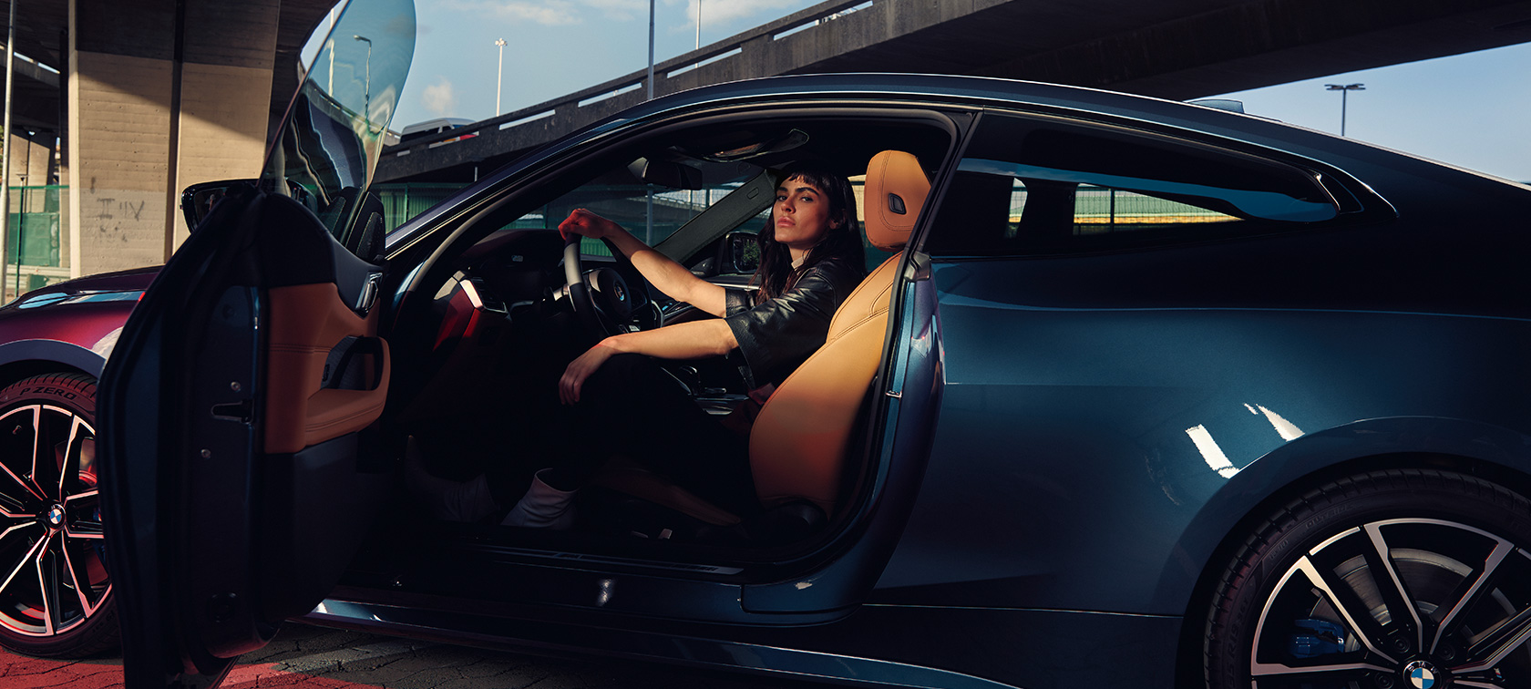 Вид BMW M440i xDrive Coupe G22 (2020) сбоку BMW M440i xDrive Coupe G22 (2020), Синий Арктик Рэйс металлик, модел сидит в автомобиле с открытой дверью, вид сбоку