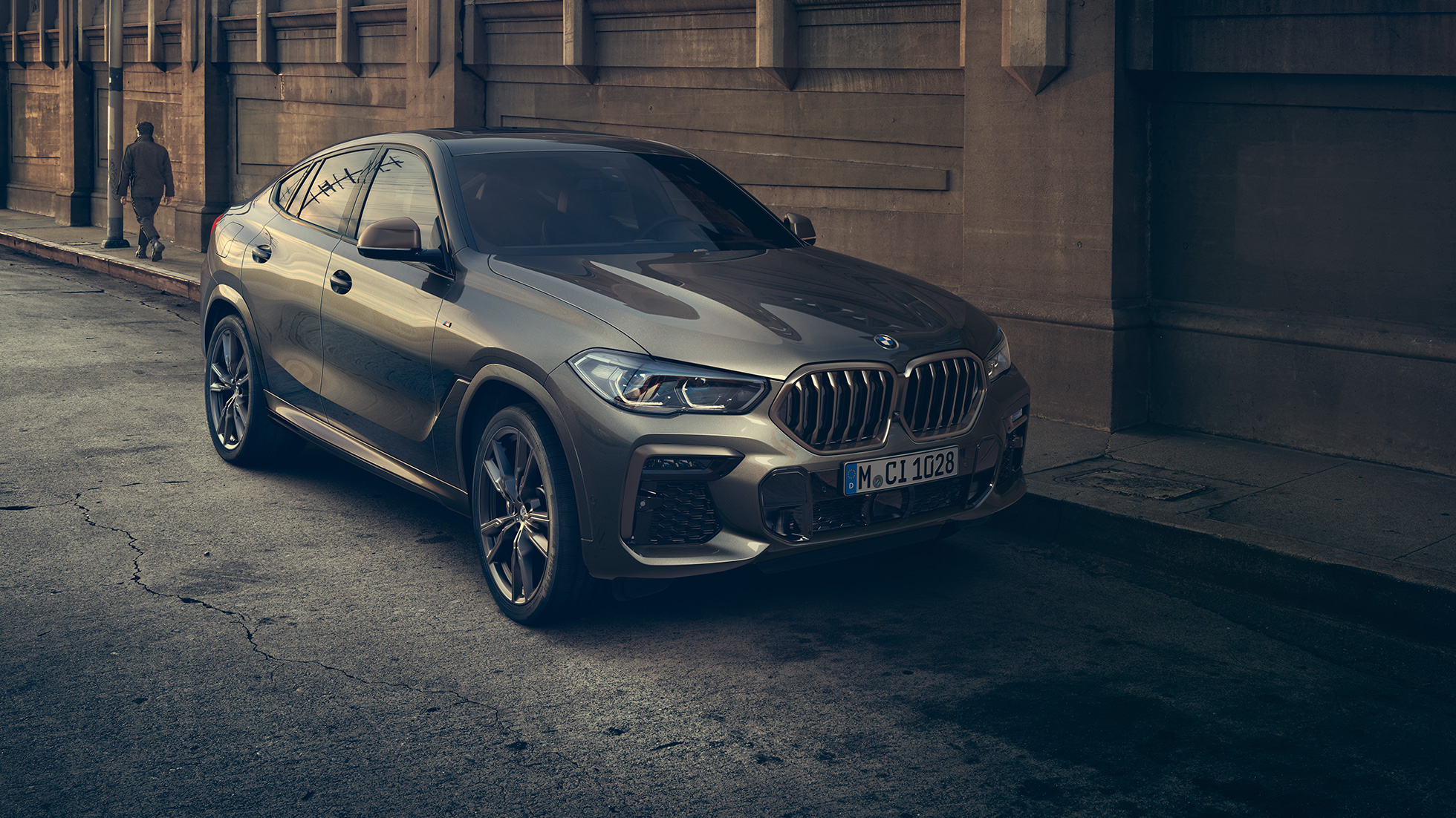 Неподвижный BMW X6 M50i. BMW X6 M50i: вид спереди с поворотом в три четверти на фоне городского пейзажа.