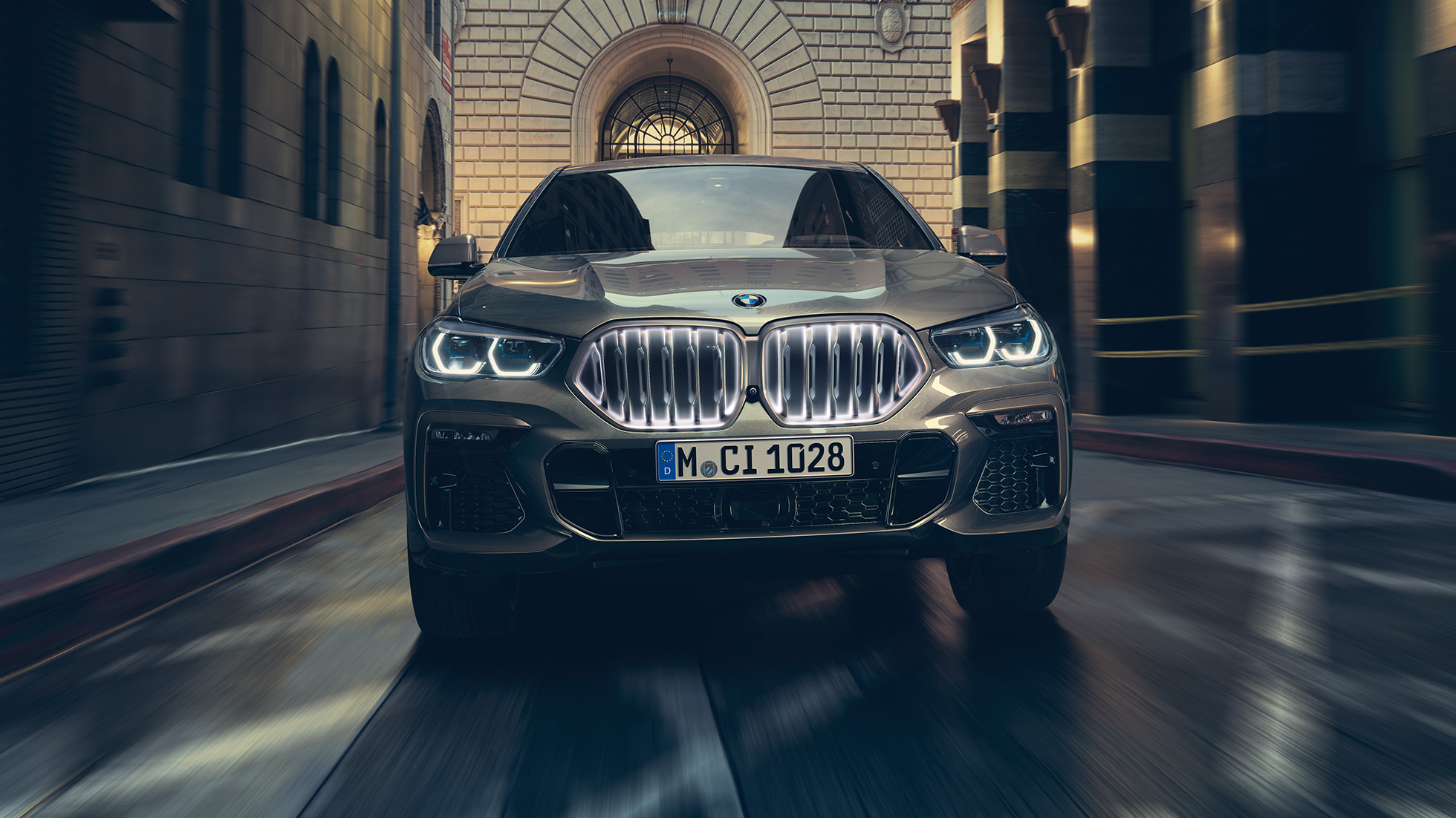 BMW X6 M50i: решетка радиатора BMW Iconic Glow. BMW X6 M50i: вид спереди на фоне городского пейзажа.