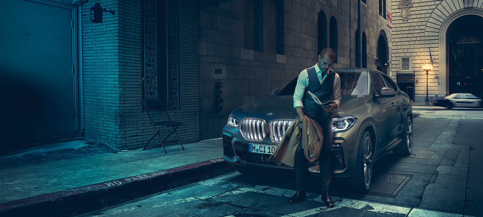 Передняя часть BMW X6 M50i Мужчина, опирающийся на переднюю часть BMW X6 M50i