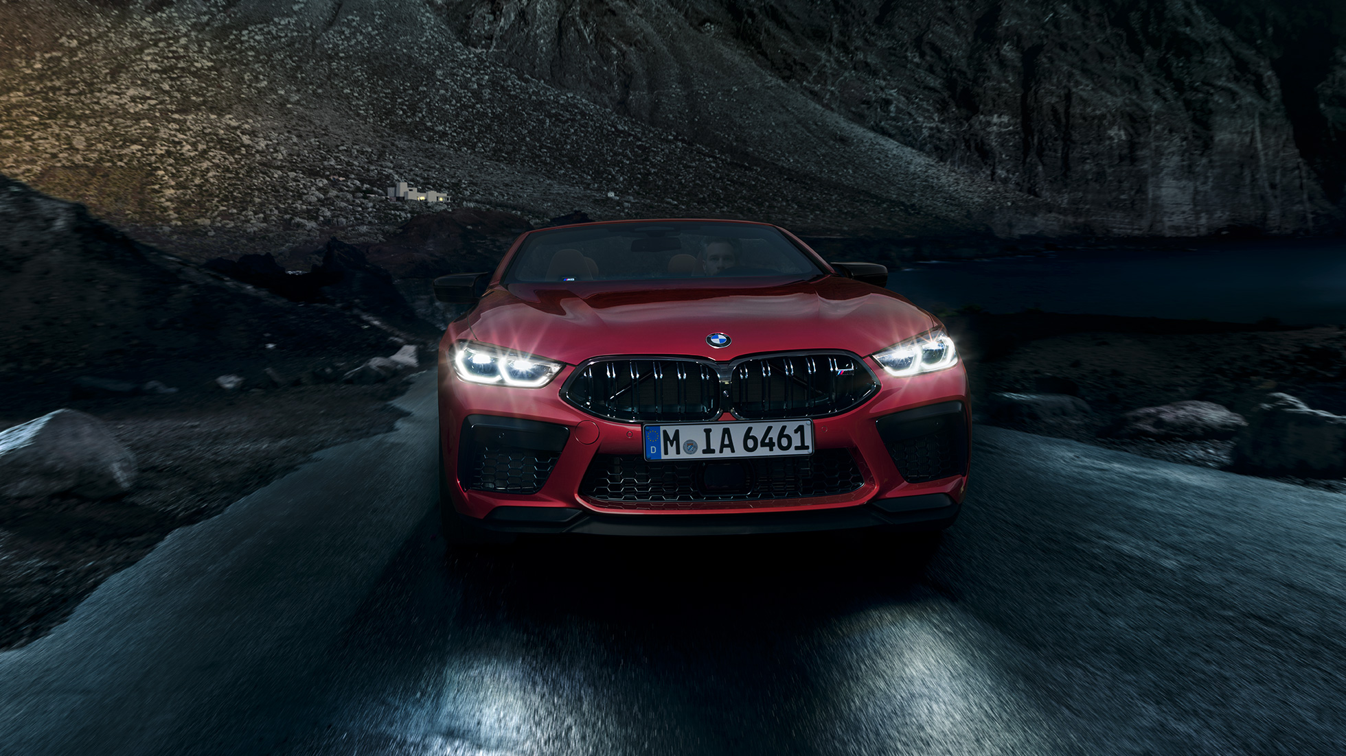 BMW M8 Competition Cabrio, вид спереди. BMW M8 Competition Cabrio с включенными фарами, Красный Мотеги металлик, вид спереди, автомобиль в движении в темное время суток.