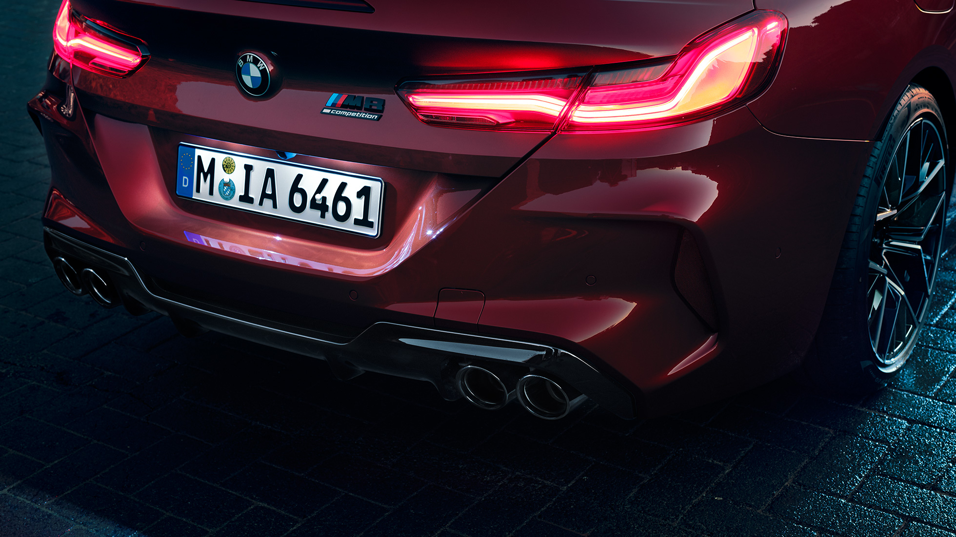 BMW M8 Competition Cabrio, крупный план задней части кузова. BMW M8 Competition Cabrio, Красный Мотеги металлик, крупный план задней части кузова с акцентом на светодиодные задние фонари и эмблему M8 Competiton.