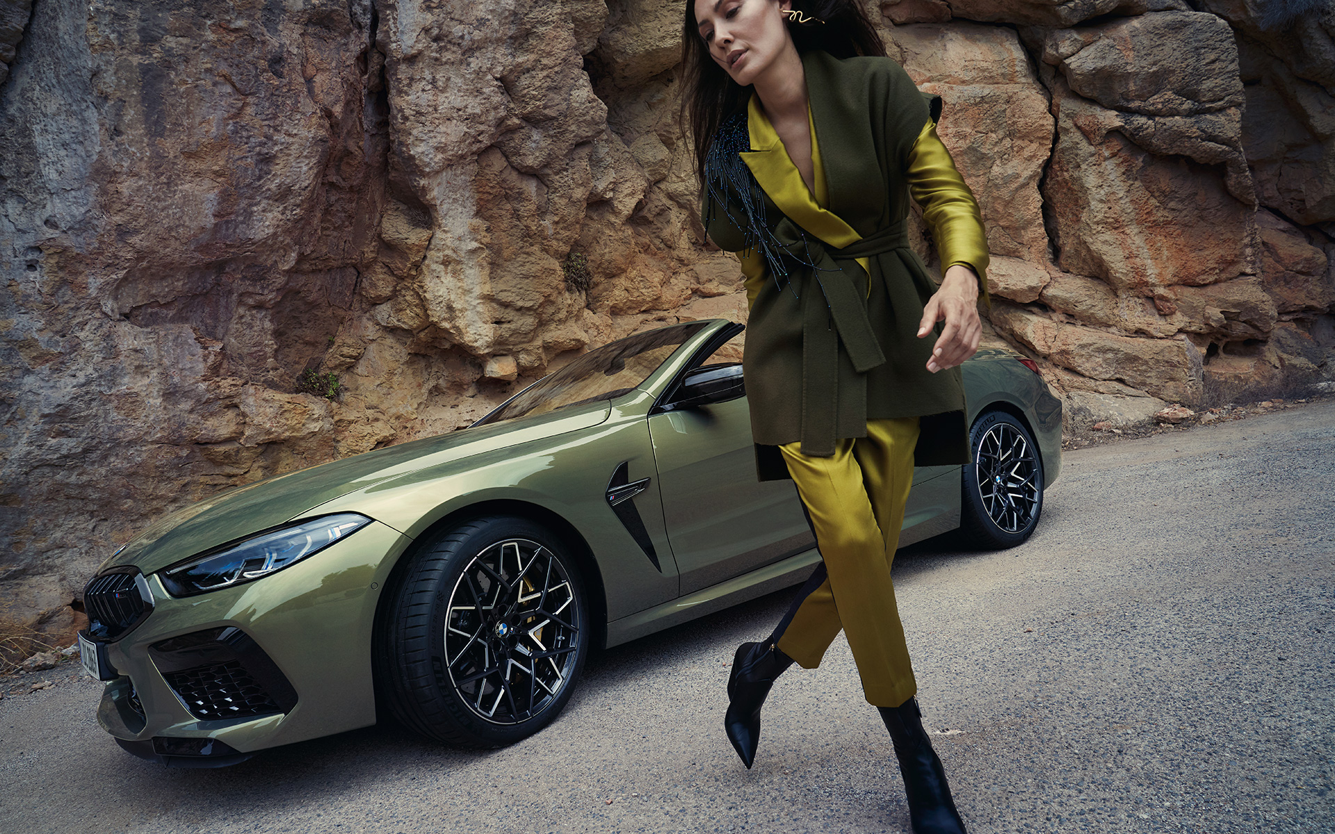 BMW M8 Competition Cabrio F91 LCI 2022, вид спереди в три четверти на каменистой местности BMW M8 Competition Cabrio F91 LCI Facelift 2022 BMW Individual Brass metallic, вид спереди в три четверти на каменистой местности с женщиной