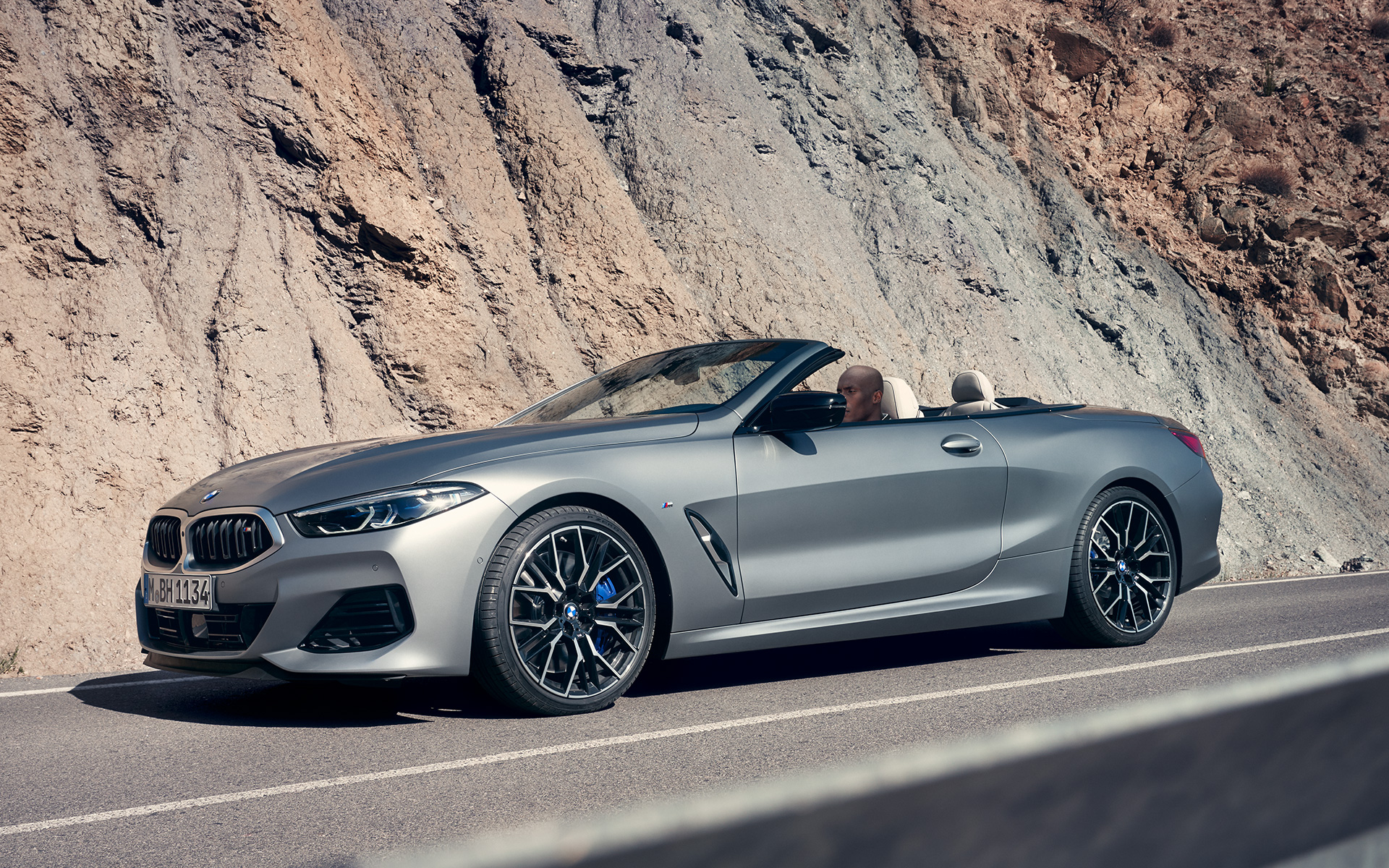 Вид спереди в три четверти BMW M850i xDrive Cabrio G14 LCI Facelift 2022 BMW M850i xDrive Cabrio G14 LCI Facelift 2022, BMW Individual Морозный Чистый Серый металлик, вид спереди в три четверти в движении на фоне скалы