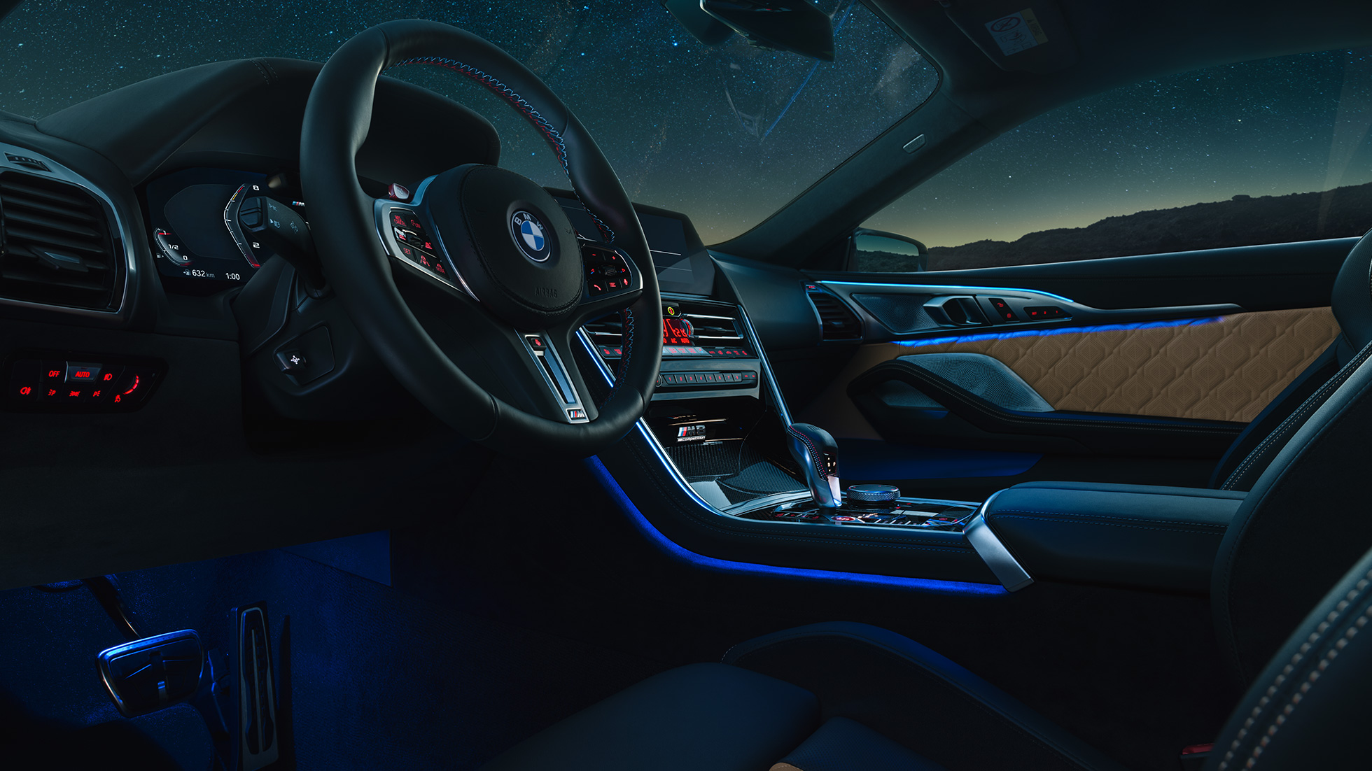 BMW M8 Competition Купе, кокпит. BMW M8 Competition Купе, кокпит с обтянутым кожей рулевым колесом M и фоновой подсветкой синего цвета в темное время суток.