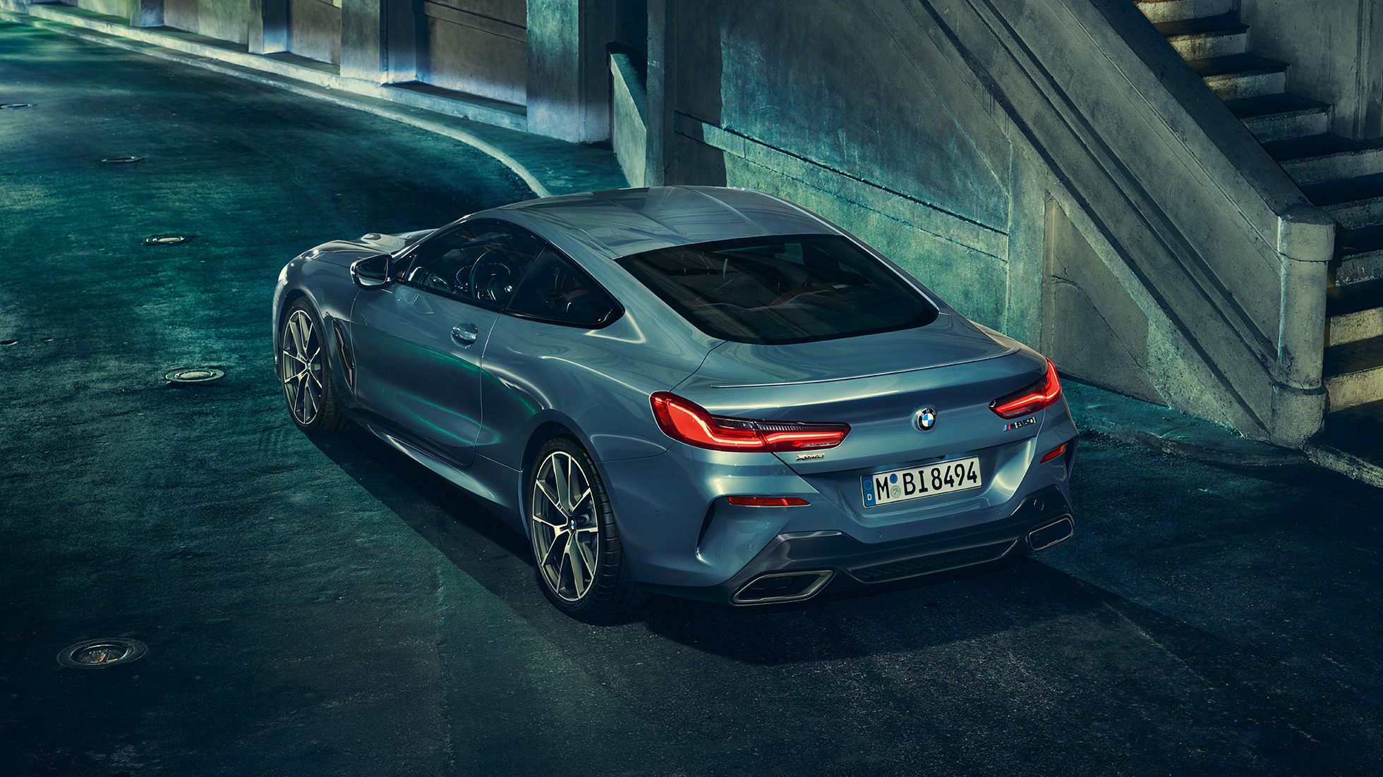 BMW M850i xDrive Coupe, вид сзади слева с поворотом в три четверти. BMW M850i xDriveCoupe, Синий Барселона металлик, вид сзади слева с поворотом в три четверти, неподвижный автомобиль в темное время суток.