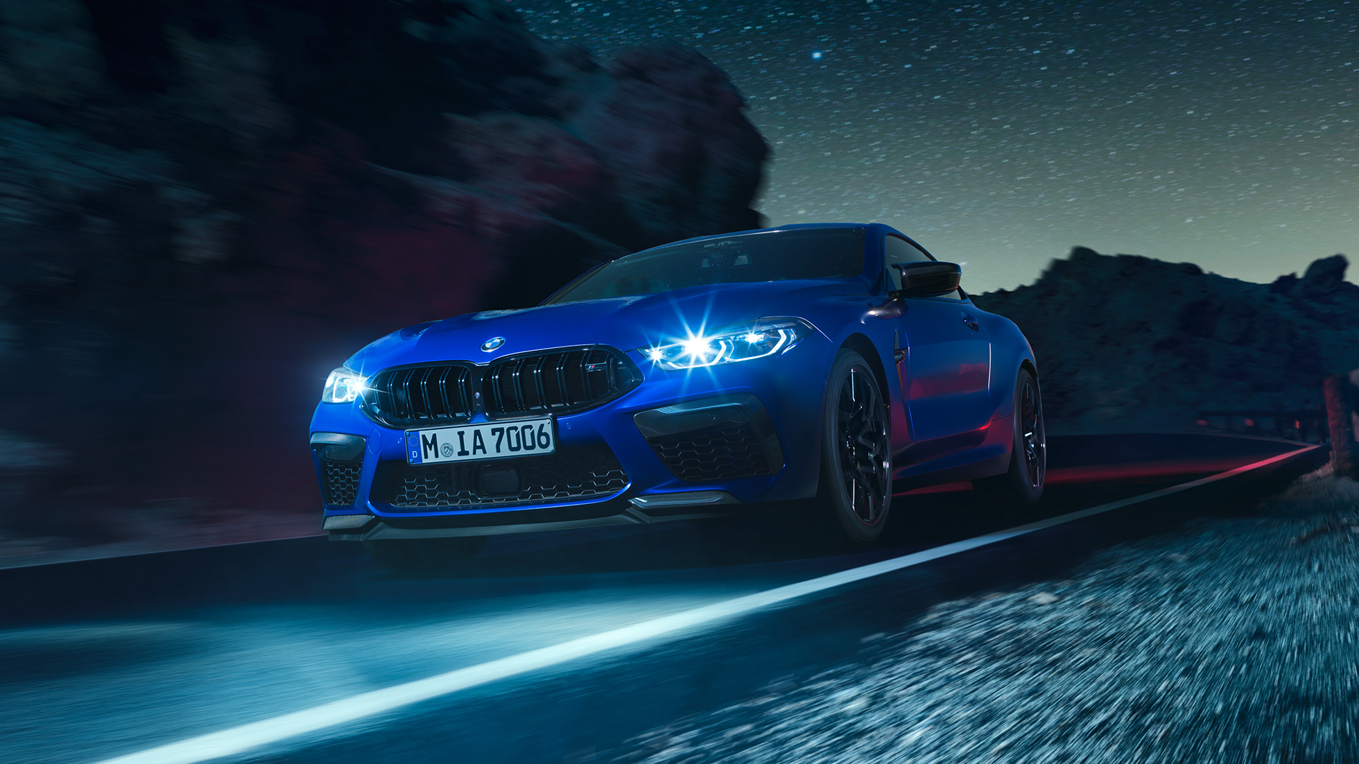 BMW M8 Coupe Competitionв движении, вид спереди с поворотом в три четверти. BMW M8 Coupe Competitionс включенными светодиодными фарами, Синий Марина Бэй металлик, вид спереди с поворотом в три четверти, автомобиль в движении в темное время суток.