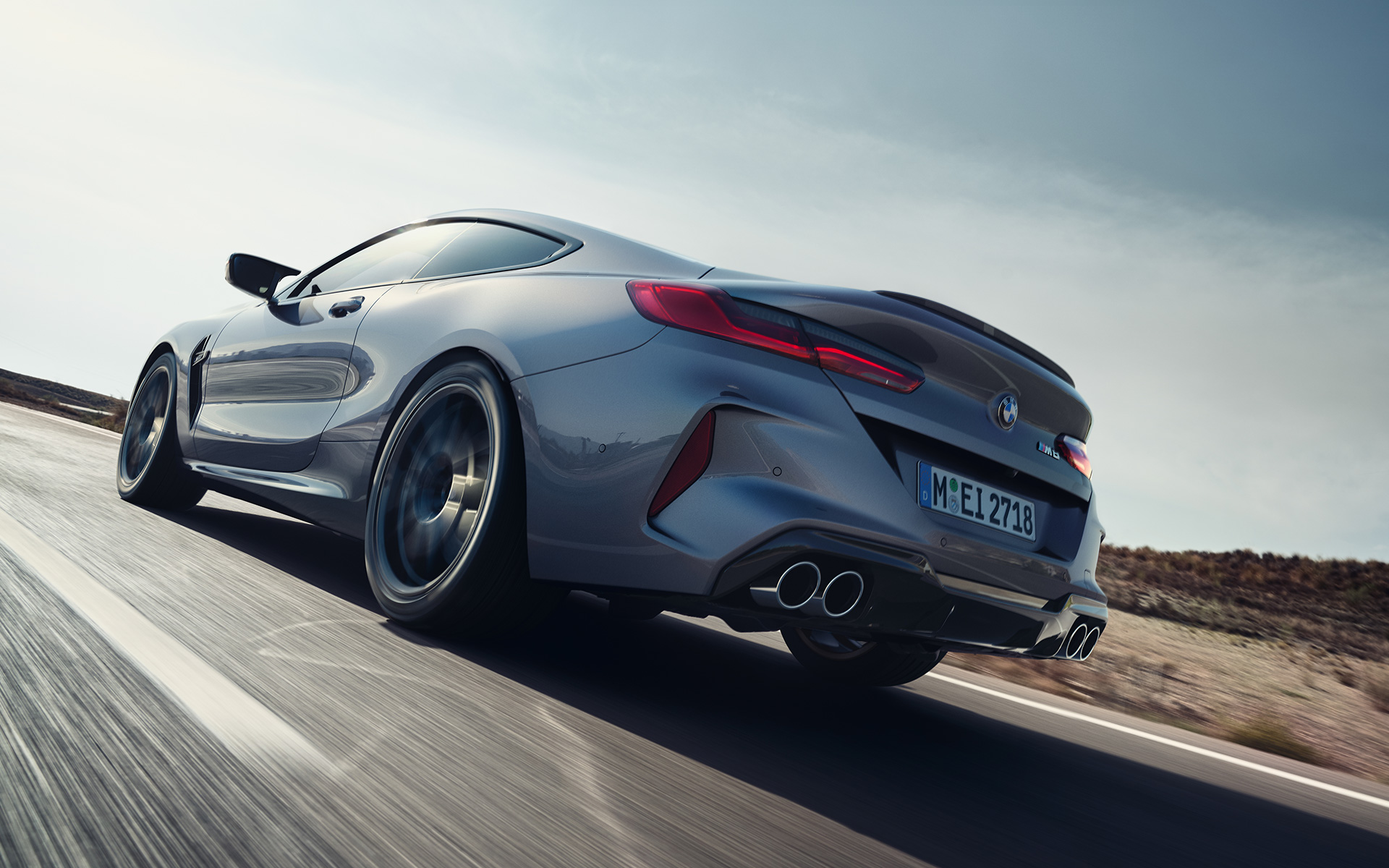 Вид сзади в три четверти BMW M8 Coupe F92 LCI Facelift 2022 в движении на магистрали BMW M8 Coupe F92 LCI Facelift 2022, "Серый Графит металлик", вид сзади снизу в три четверти в движении на магистрали