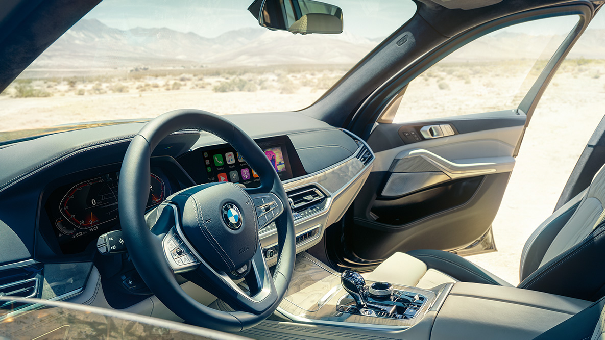 Интерьер BMW X7 Интерьер BMW X7: вид снаружи на первый ряд сидений с охватом рулевого колеса, приборной панели и кожаных сидений
