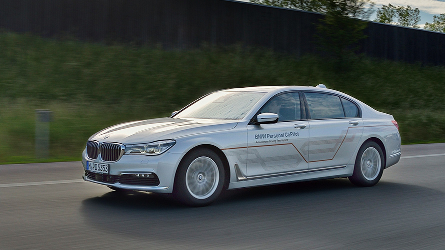 BMW Personal CoPilot: экспериментальный парк автомобилей для испытания систем автономного вождения сегодня Седан BMW 5-й серии серого цвета с надписью BMW Personal CoPilot, движется по шоссе (вид слева).