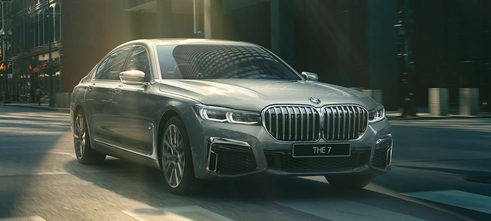BMW 7 серии серого цвета в движении по городским улицам: вид спереди с поворотом в три четверти G11 Седан BMW 7 серии серого цвета в движении: вид спереди с поворотом в три четверти G11