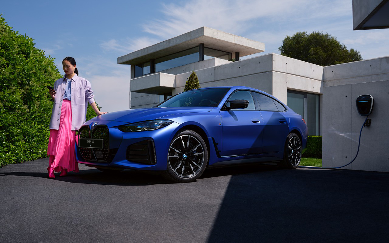 BMW i4 M50 G26 2021 &quot;Морозный Синий Портимау металлик&quot; BMW Individual, вид спереди в три четверти с женщиной перед домом
