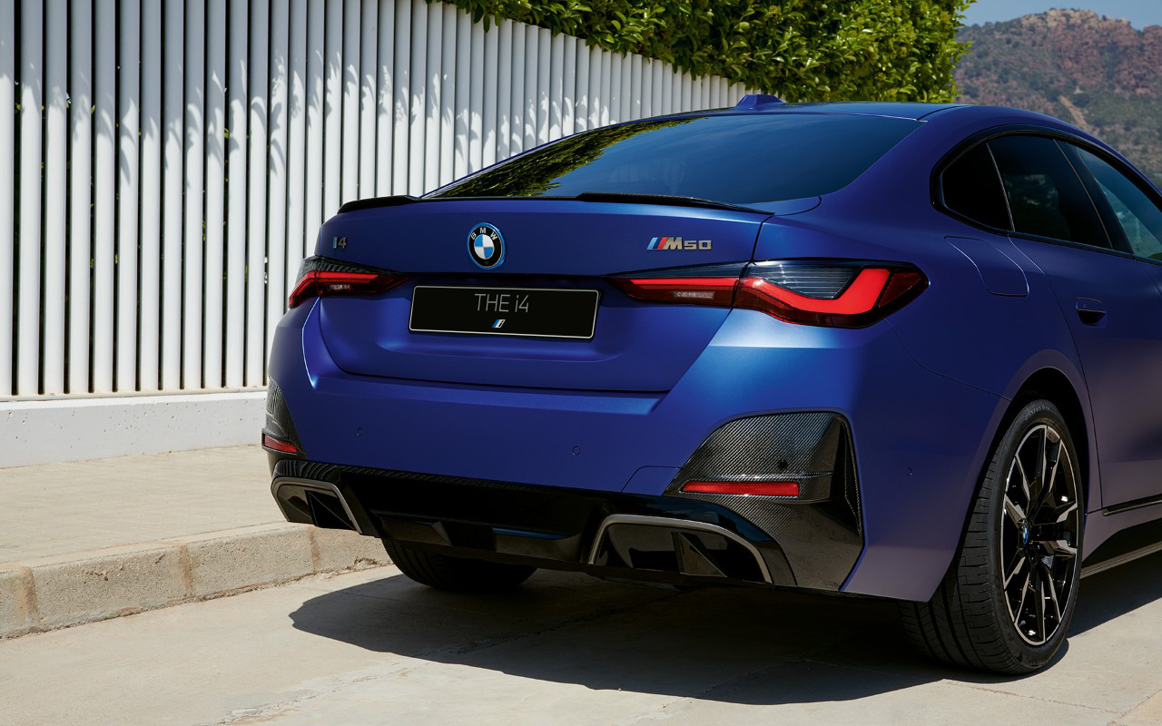 BMW i4 M50 G26 2021 &quot;Морозный Синий Портимау металлик&quot; BMW Individual, вид сзади в три четверти в статике у белого ограждения