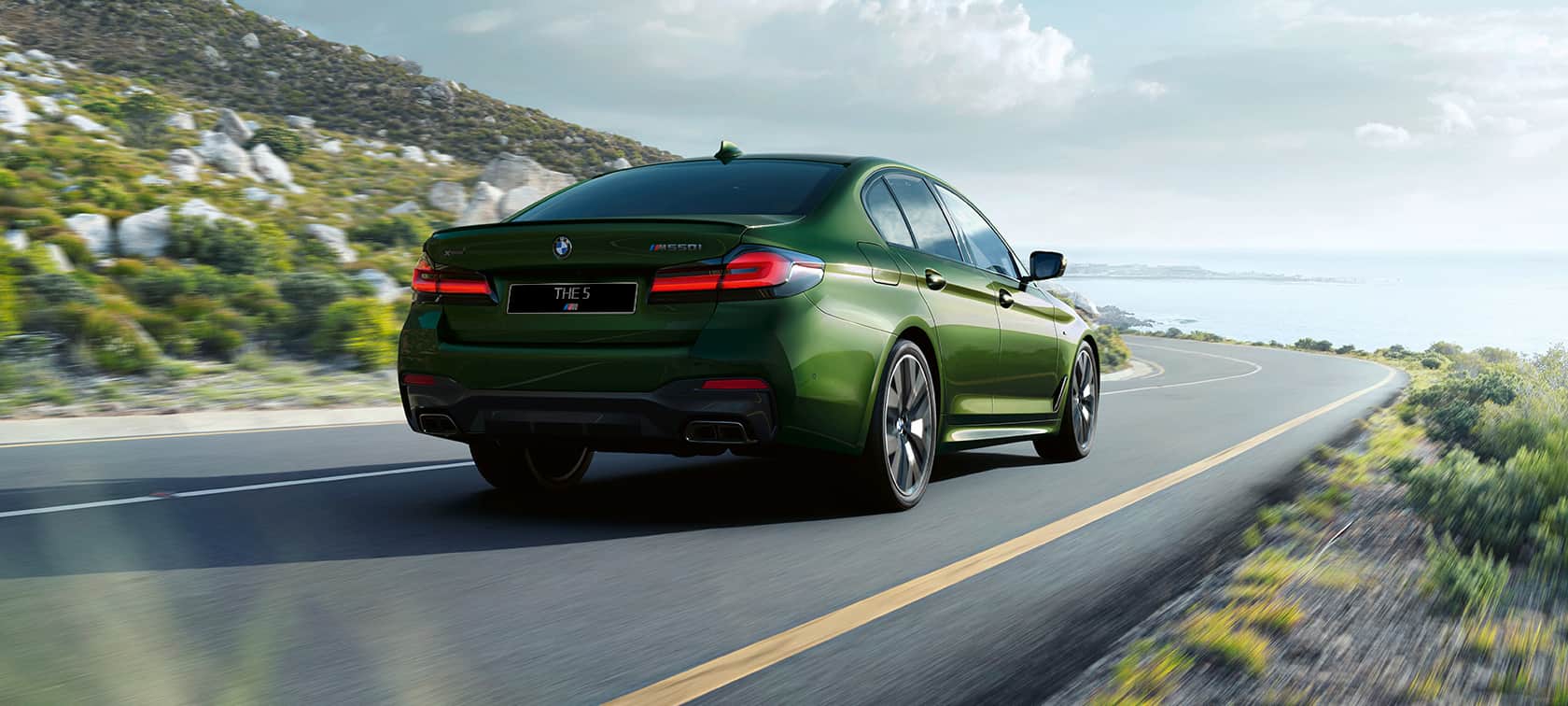 BMW M550i xDrive G30 LCI Facelift 2020, вид сзади в три четверти, в движении BMW M550i xDrive G30 LCI Facelift 2020, BMW Individual "Зеленый Эрмес металлик", вид сзади в три четверти, в движении