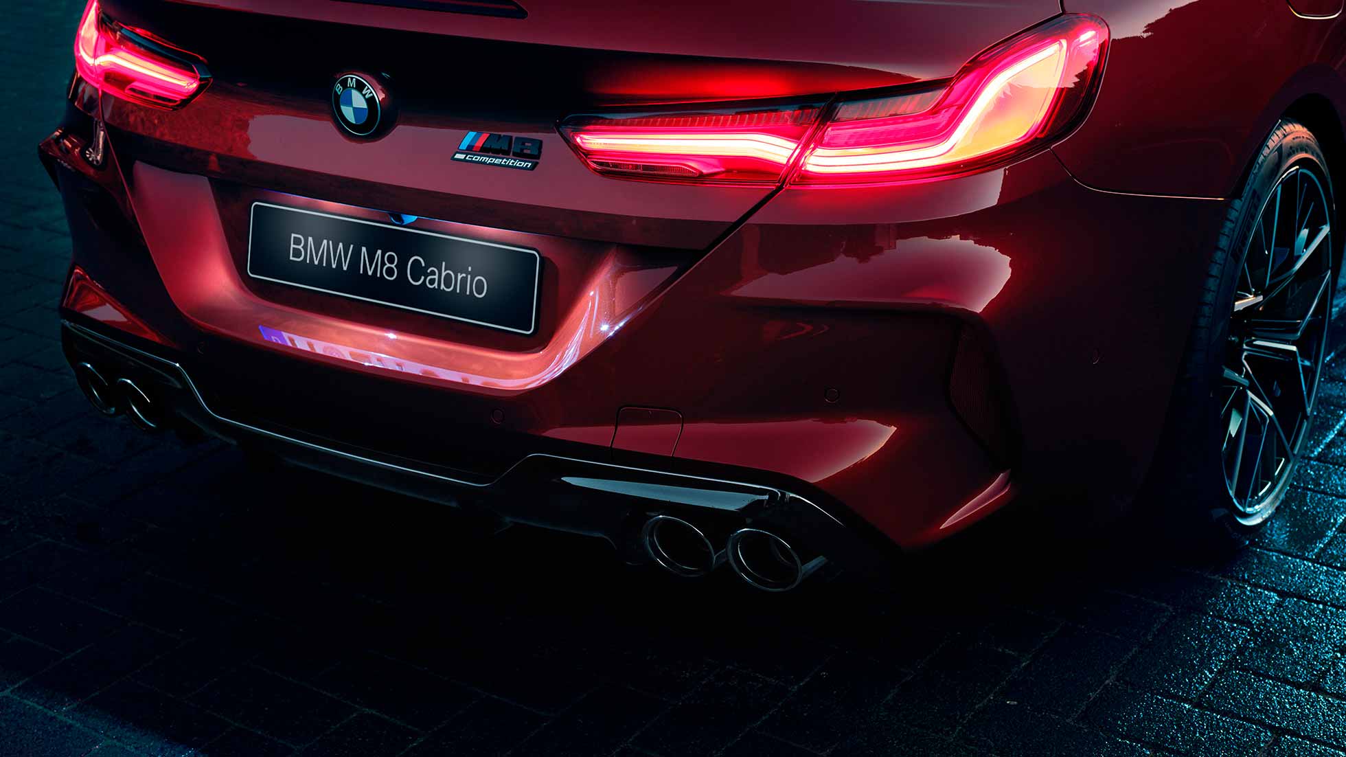 BMW M8 Competition Cabrio, крупный план задней части кузова. BMW M8 Competition Cabrio, Красный Мотеги металлик, крупный план задней части кузова с акцентом на светодиодные задние фонари и эмблему M8 Competiton.