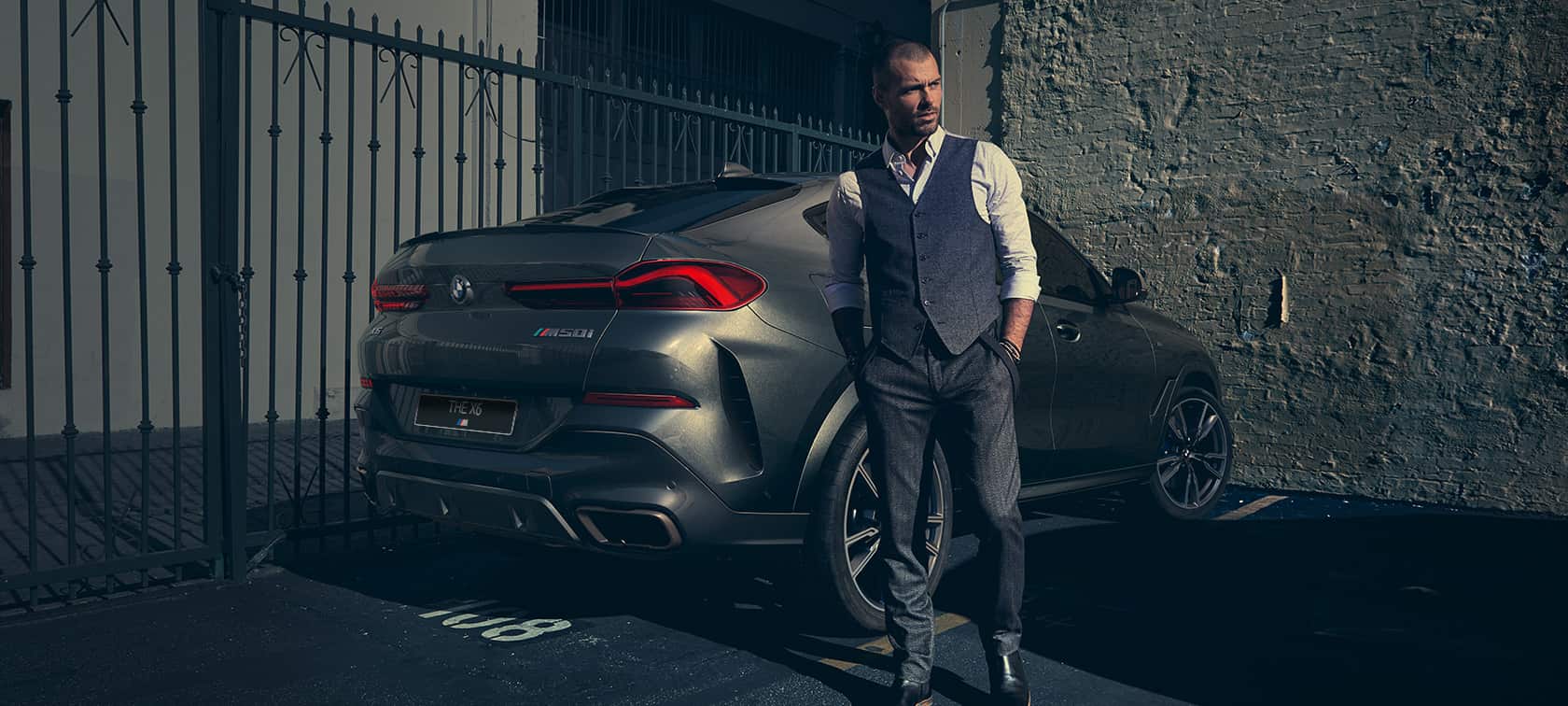 BMW X6 M50i SUV, вид сзади с поворотом в три четверти F86. Мужчина стоит рядом с BMW X6 M50i SUV, вид сзади с поворотом в три четверти F86