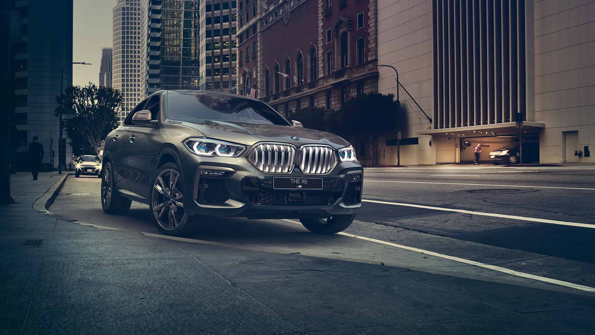 Неподвижно стоящий BMW X6 M50i SUV F86 BMW X6 M50i SUV: вид спереди с поворотом в три четверти на фоне городского пейзажа F86