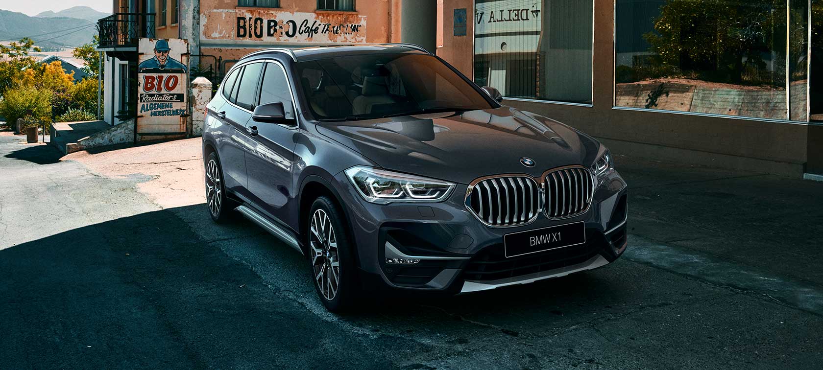 BMW X1 SUV, вид спереди с поворотом в три четверти F48. BMW X1 SUV, вид спереди с поворотом в три четверти на фоне городского пейзажа F48.